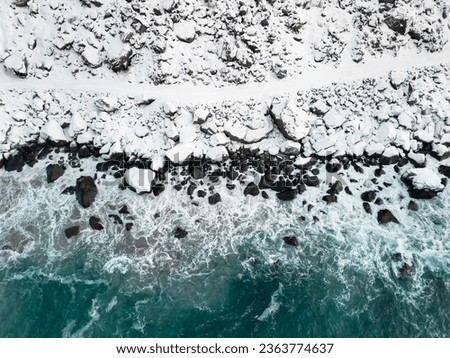 Path in the snow next to a wild shore with waves of blue ocean. Aerial view of dangerous winter pathway in Norway. Royalty-Free Stock Photo #2363774637