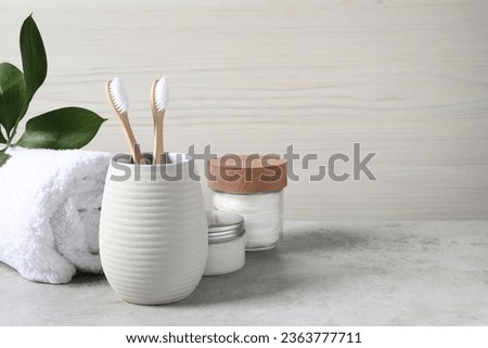 Bamboo toothbrushes in holder, towel, cotton pads and cream on light grey table, space for text
