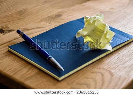 Notebook for writing notes. Lined notebook with blue boards and yellow pages with blue lines. With a blue pen for writing. A crumpled piece of paper.
