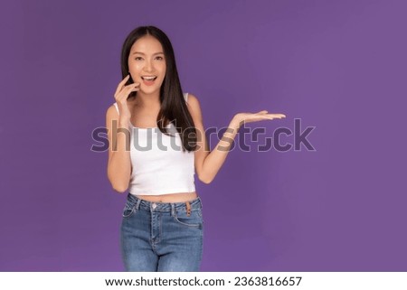 Beautiful Asian brunette woman cute girl in white tank top smiling and posing her empty hands with copy space for present product or blank space for advertising isolated on purple background
