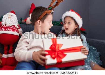 Adorable boy and girl unpacking christmas gift sitting on sofa at home