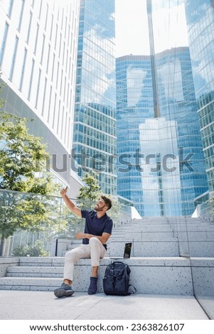Handsome man taking selfie on phone sitting on stairs on modern city background