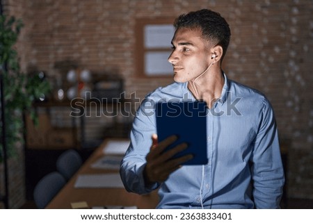 Handsome hispanic man working at the office at night looking to side, relax profile pose with natural face and confident smile. 