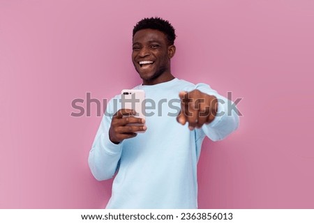 I choose you. african american man using smartphone laughing and pointing with his hand at the camera on pink isolated background, the man makes fun and takes pictures on the camera