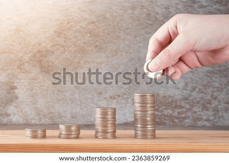 Stack of coins and boy's hand holding coins on wooden background. Concepts of finance, banking, education and economics. Royalty-Free Stock Photo #2363859269