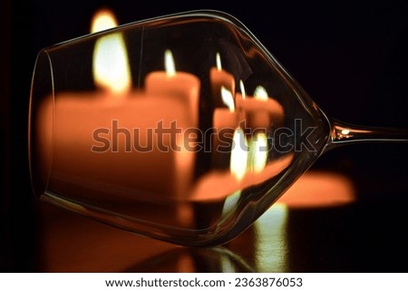 An empty wine glass on top of a black table with some candles on the back