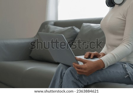 Woman holding credit card using laptop and mobile phone to shop online on sofa in living room at home
