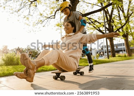 Cheerful african american boy wearing safety helmet riding his mother on skateboard in sunny park