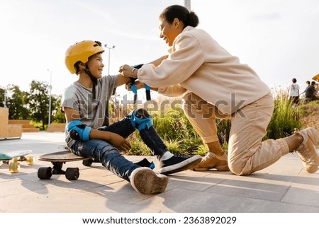 Smiling african american mother putting safety gear on her cute little son at skatepark