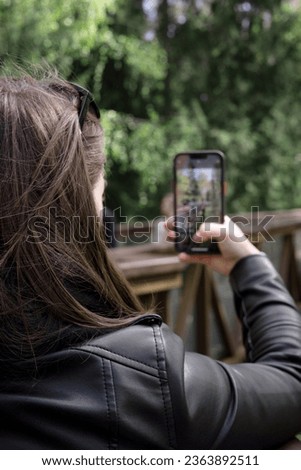 A young girl holds a phone in her hands and takes pictures of nature. View from the girl's shoulder. Dark hair, autumn landscape.