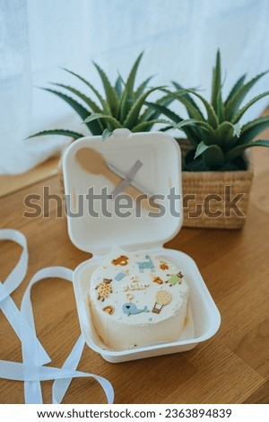 Birthday cake for 1 year child with painted cartoon animals on it. Wooden table with plants and cake on it. Vertical shoot of cute cake.