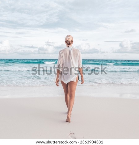 Woman wearing white loose tunic over bikini on Mahe Island, Seychelles. Summer vacations on picture perfect tropical beach concept.