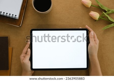 Woman hand holds digital tablet mockup with blank screen, education and application concept template, bright brown background, top view and copy space photo.