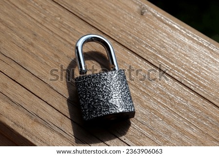 An open metal padlock lies on a wooden surface. Horizontal photo, close-up