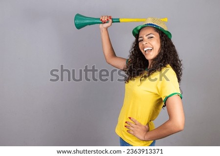 Young brazilian cheerleader with a vuvuzela on grey background celebrating