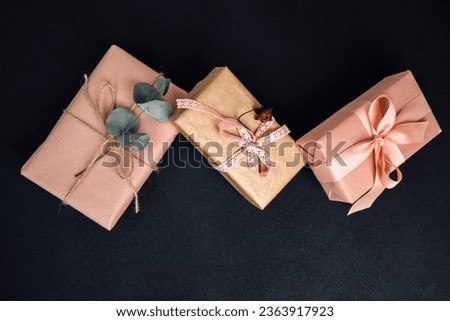 Background for greetings. Gifts wrapping in soft pink paper with dry eucalyptus branch on a black concrete background. Top view