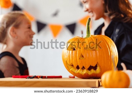 Closeup of a carved Halloween pumpkin. Mother and daughter in costumes excited about the party in the background