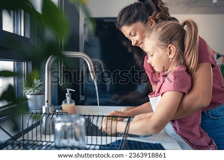 A cute little girl helps her mother washing dishes. Child doing house chores. Mother teaches a child to wash dishes. Royalty-Free Stock Photo #2363918861