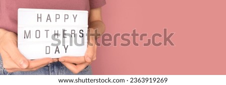 Happy Mothers Day. Banner with woman hold in hands lightbox with letters in front of pink background. 
