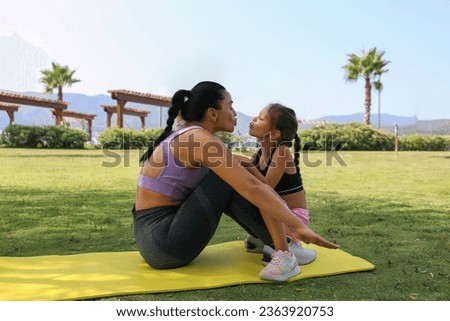 Mother and daughter spending quality time together, bonding through physical exercise. Little girl joined her mom for a morning exercise, doing sit ups in the park. Close up, copy space, background.