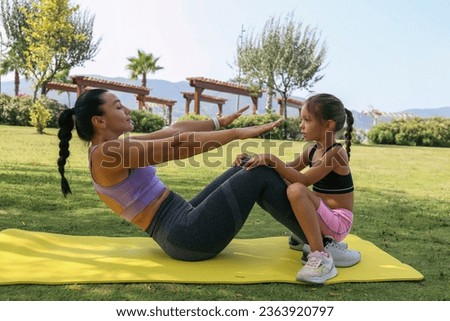 Mother and daughter spending quality time together, bonding through physical exercise. Little girl joined her mom for a morning exercise, doing sit ups in the park. Close up, copy space, background.