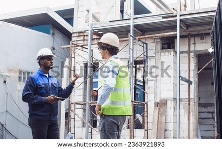 Two diversity male engineers team working, inspecting outdoor at construction site, wearing hard hats for safety, talking, discussing. Career, Industry Concept