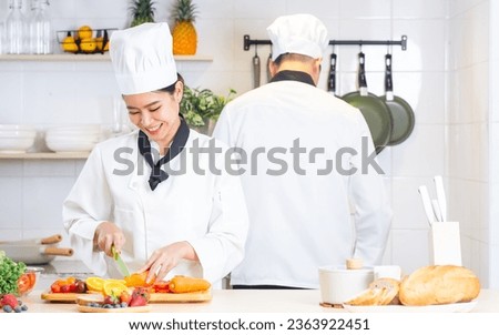 Two Asian professional couple chef wearing white uniform, hat, helping each other, preparing meal,cooking in kitchen together, smiling with happiness and confidence. Food Concept