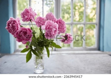 Peonies in a vase on the table against the background of the window.
