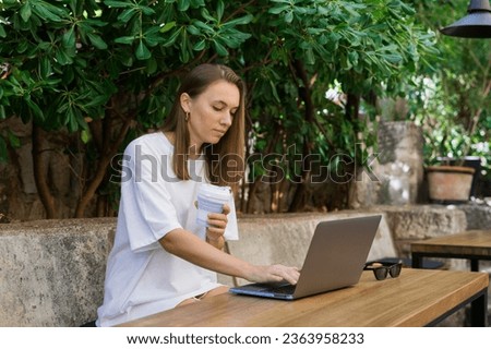 Work online. A young woman is typing on a laptop while sitting in a summer cafe. Ability to work remotely Royalty-Free Stock Photo #2363958233