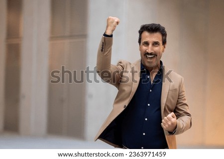 Excited happy handsome mature middle eastern man entrepreneur raising hands up and exclaiming, copy space for advertisement, businessman going by urban street city area. Business success concept Royalty-Free Stock Photo #2363971459