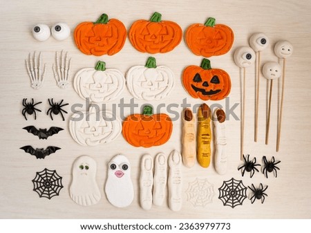 On the table there are children's crafts made from salt dough, pumpkins, witch fingers, ghosts, monsters, spiders, cobwebs, eyes, for the Halloween holiday.  Flat lay top view. 