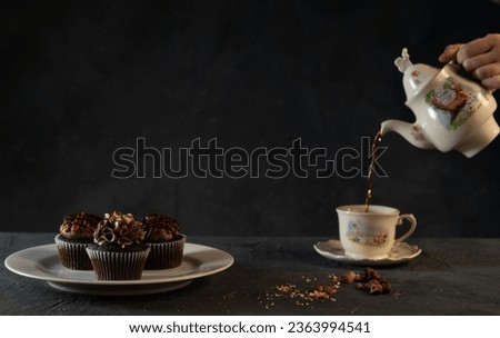 Chocolate cupcakes with frosting, and an Alice in Wonderland teaset. Set on a dark table with a dark background