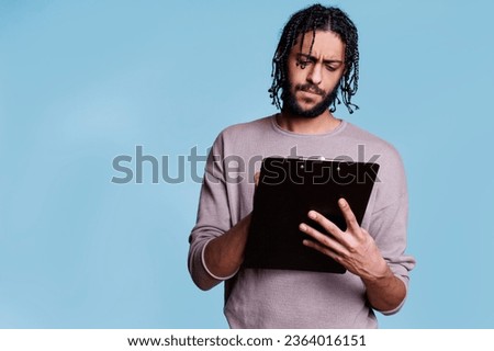 Concentrated arab writing on clipboard, filling application form with focused facial expression. Young thoughtful person standing while taking notes, reading and checking list