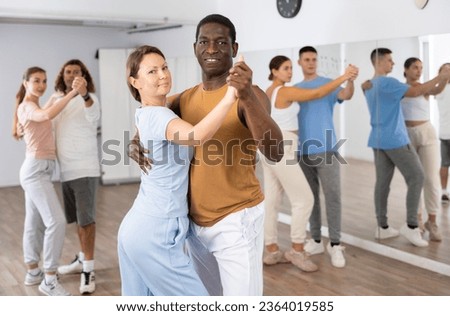Portrait of positive adult couples dancing tango together in modern studio