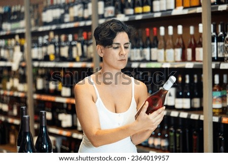 Portrait of young brunette visiting winehouse in search of bottle of good wine.. Royalty-Free Stock Photo #2364019957