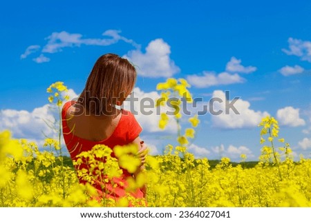 Young pretty woman in colored dress on lightning cheerful yellow background of blooming rapeseed field. Pleasure concept