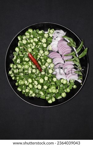 ingredients for lady finger fry chopped cut onion curry leaves red chillies black background plate