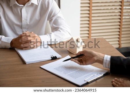 Female real estate agent in suit negotiating about house price, finance, and agreement with buyer or client at desk showing document detail and information before signing contract. Business, mortgage,