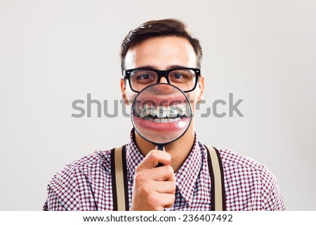 Nerdy man is holding loupe and showing his teeth with braces.I have braces and I am still handsome! Royalty-Free Stock Photo #236407492