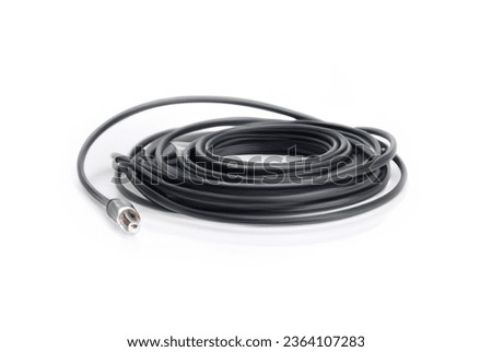The cable is black with the connector white. The cable is located on a white table. In the background, there is a white wall.