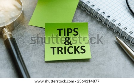 Magnifying glass and notebook with TIPS AND TRICKS word with copy space on gray table. tips and tricks concept