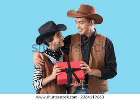 Little boy and his father dressed for Halloween as cowboys with gift on blue background