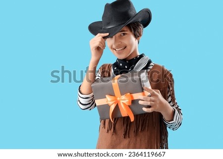 Little boy dressed for Halloween as cowboy with gift on blue background