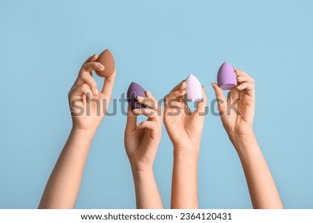 Female hands with different makeup sponges on blue background Royalty-Free Stock Photo #2364120431