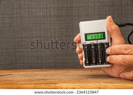 Four rechargeable batteries in a battery charger. Hands placing a battery in a charger with a green display showing the level of charge. NI-MH and LI-MH lithium battery. Copy space. Royalty-Free Stock Photo #2364125847