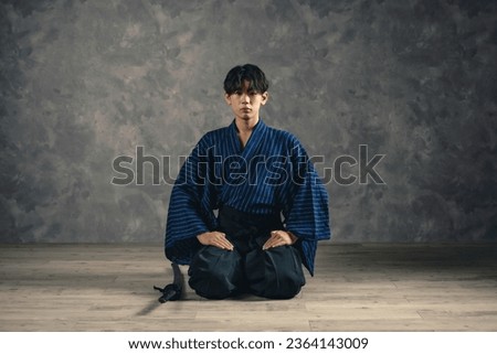 A young Japanese man wearing a kimono and sitting on a stage. Royalty-Free Stock Photo #2364143009