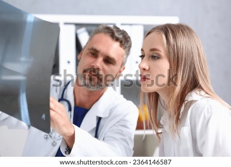 Mature male doctor hold in arm and look at xray photography discussing it with female patient portrait. Bone disease exam medic assistance cancer test healthy lifestyle hospital practice concept