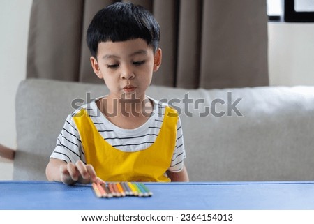 Cheerful little child boy in striped yellow shirt looking and try to choose a color pencils on desk. Education and school concept.