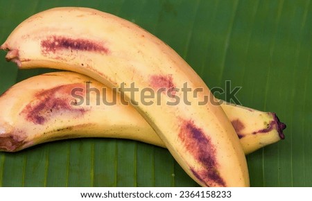a photography of two bananas on a banana leaf on a table, banana with brown spots on it sitting on a banana leaf.