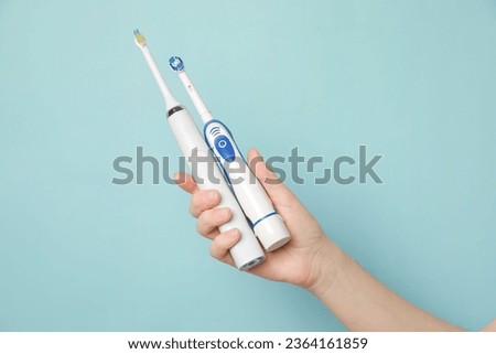 Woman holding electric toothbrushes on light blue background, closeup